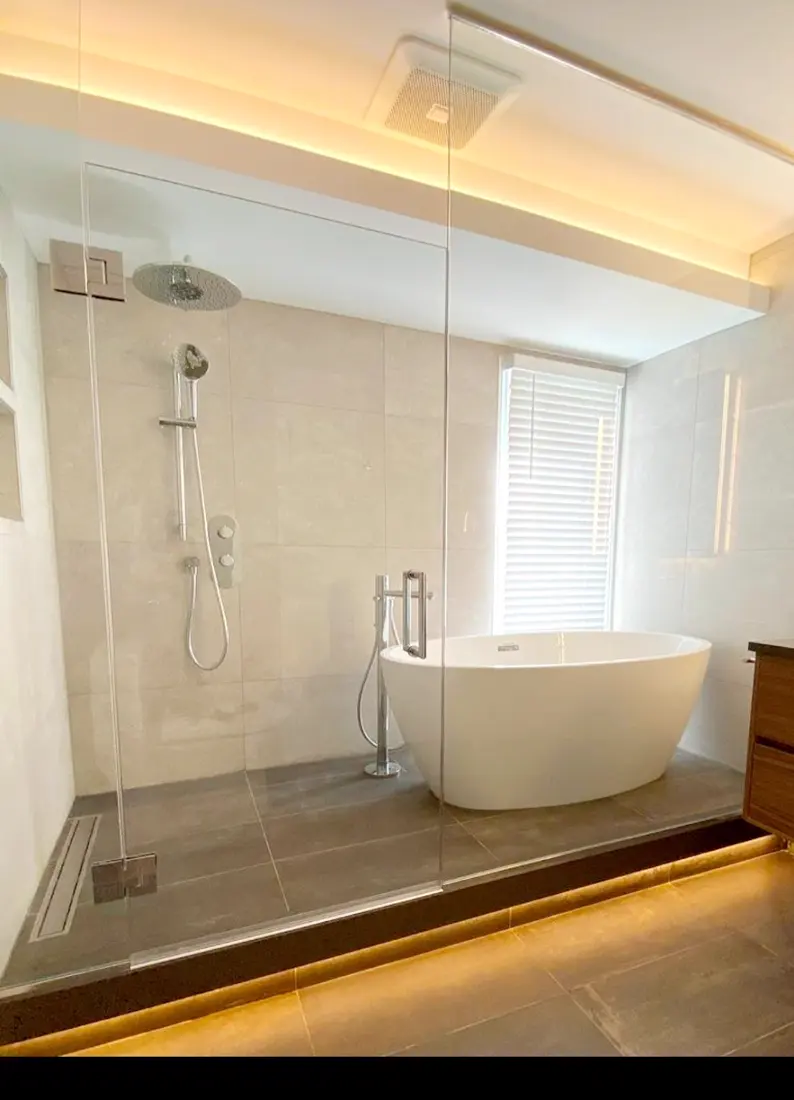Salle de bain avec bain autoportant derrière une paroi vitrée et éclairage indirect