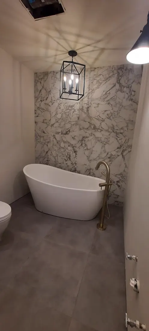 Bain autoportant devant un mur effet marbre sous un luminaire lanterne